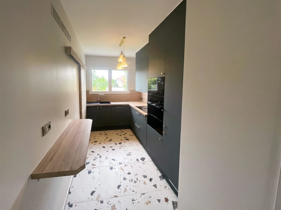 Cuisine moderne en L rénovée, sol en terrazzo, meubles bas et colonnes en gris anthracite mat, plan de travail en bois stratifié, crédence imitation chêne
