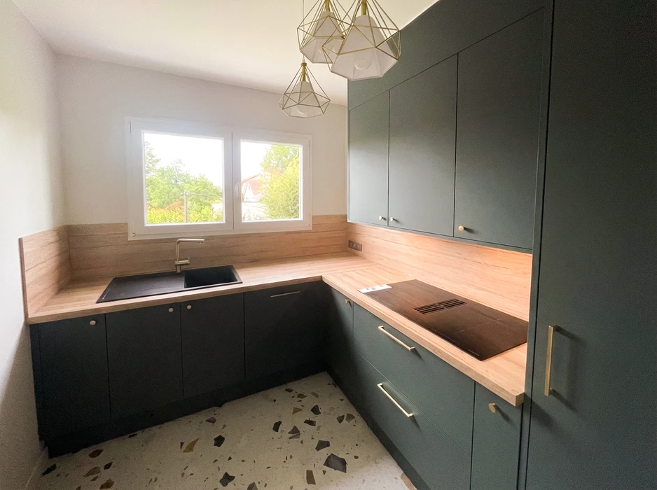 Cuisine rénovée en L, meubles façades vert sapin mat, plan de travail et crédence en bois clair stratifié