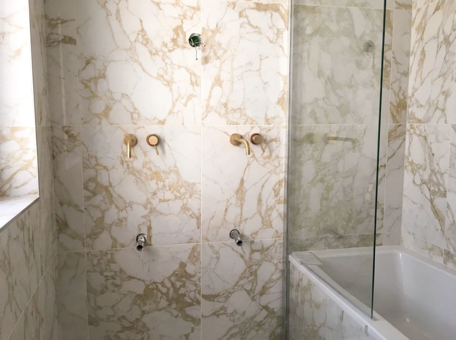 Salle de bains luxueuse avec carrelage grand format effet marbre Calacatta Gold, veinage beige doré sur fond blanc